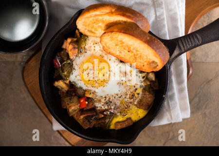 Breakfrast hash in Gusseisen Skillet mit sunny side up gebratene Eier, Schinken, Pilze, würzige Paprika, Kartoffeln, Toast und Kaffee. Stockfoto