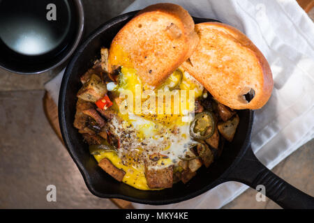 Breakfrast hash in Gusseisen Skillet mit sunny side up gebratene Eier, Schinken, Pilze, würzige Paprika, Kartoffeln, Toast und Kaffee. Stockfoto