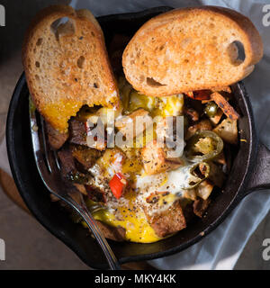 Breakfrast hash in Gusseisen Skillet mit sunny side up gebratene Eier, Schinken, Pilze, würzige Paprika, Kartoffeln, Toast und Kaffee. Stockfoto