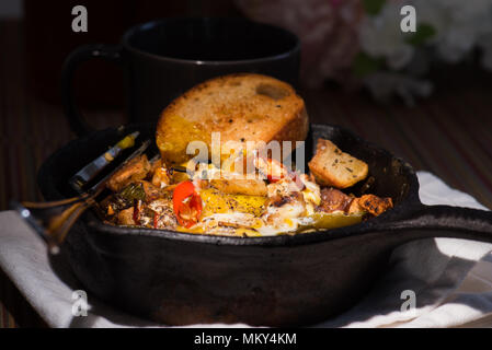 Breakfrast hash in Gusseisen Skillet mit sunny side up gebratene Eier, Schinken, Pilze, würzige Paprika, Kartoffeln, Toast und Kaffee. Stockfoto