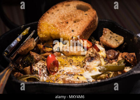 Breakfrast hash in Gusseisen Skillet mit sunny side up gebratene Eier, Schinken, Pilze, würzige Paprika, Kartoffeln, Toast und Kaffee. Stockfoto