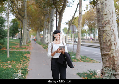 Schöne schwarze Mädchen zu Fuß nach Klassen mit Tablet auf der Straße mit Laub. Stockfoto