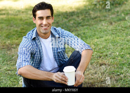 Mann mit legere Kleidung trinken Kaffee in einem städtischen Park zu gehen. Mann, blau karierte Hemd und Jeans. Stockfoto