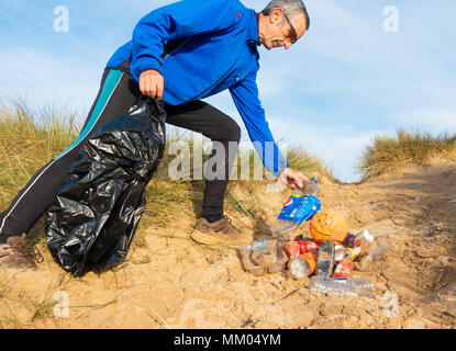 Ein Jogger Plogging (Abholung Wurf beim Joggen) auf seinen Morgen durch Sanddünen. DE Stockfoto