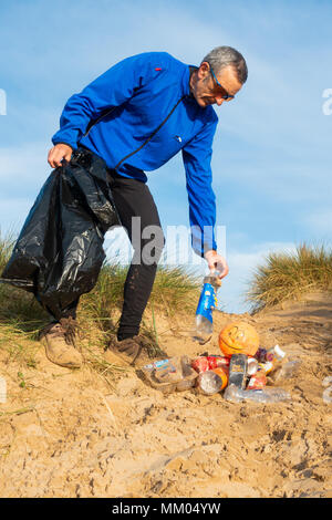 Ein Jogger Plogging (Abholung Wurf beim Joggen) auf seinen Morgen durch Sanddünen. DE Stockfoto