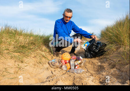 Ein Jogger Plogging (Abholung Wurf beim Joggen) auf seinen Morgen durch Sanddünen. DE Stockfoto