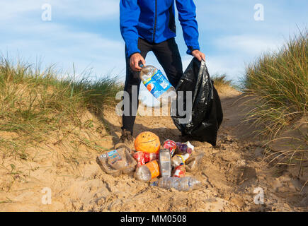 Ein Jogger Plogging (Abholung Wurf beim Joggen) auf seinen Morgen durch Sanddünen. DE Stockfoto