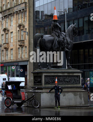 Glasgow, Schottland, Großbritannien 9. Mai. Glasgow, Schottland, Großbritannien 9. Mai - leitkegel Royal Exchange Square Herzog von Wellington Statue. Den Kegel Mann in der Stadt Goma, Museum für moderne Kunst ist ein Symbol wie Glasgow. s Nur vollen Tag Zeit Bike Taxi für Touristen und Einheimische gleichermaßen Tom Brown und seinen Zyklus Rikscha im Herzen der Stadt so stumpf nasses Wetter zieht nach dem heißen Bank Urlaub.. Gerard.. Gerard Fähre / alamy Nachrichten Stockfoto