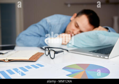 Stressvolle männlichen Schlafen auf der Tabelle mit Laptop und Dokumente. Sleepworking nach langen Quark Aufwand Stockfoto