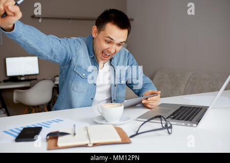Junger Mann schaut auf Laptop- und der Beifall aus, was er sah. Händler überwachung Börse. Stockfoto