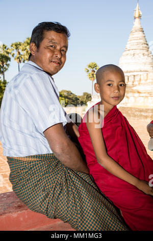 Bagan, Myanmar, 29. Dezember 2017: Vater und Sohn als ein buddhistischer Novize sitzen vor einer Pagode in Bagan, Myanmar lächelnd Stockfoto