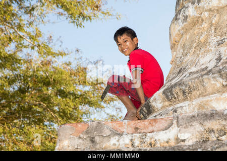 Bagan, Myanmar, 29. Dezember 2017: lächelnde Junge mit Tanaka im Gesicht sitzt am Fuße eines Stupa in Bagan, Myanmar Stockfoto