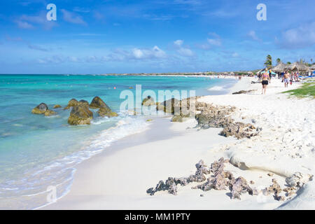 Arashi Beach, Aruba, Karibik im Januar 2018: Touristen entspannen unter Sonnenschirmen oder Baden im türkisfarbenen Wasser. Stockfoto
