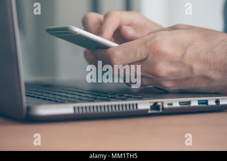 Nahaufnahme der männlichen Händen zwischen Smartphone und Laptop Computer im Business Office, moderne Funktechnologie Stockfoto