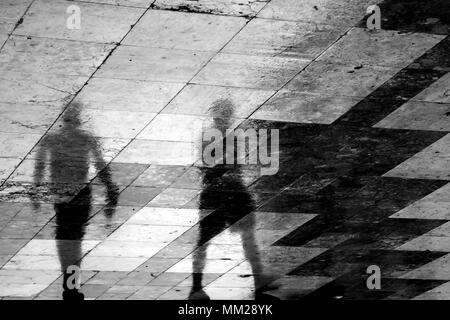 Unscharfe Reflexion Schatten von zwei Menschen zu Fuß die Stadt Straße gemusterten Bürgersteig an einem regnerischen Frühlingstag Stockfoto