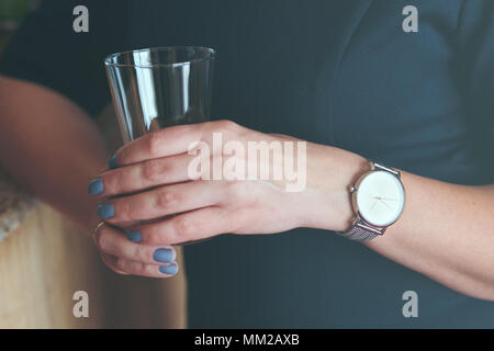 Elegante Frau tragen Silber Armbanduhr und blauen Kleid holding Glas Wasser Stockfoto