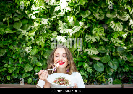 Junge und schöne Frau mit gesunden Salat an das vegetarische Restaurant sitzen mit Living Wall der grünen Pflanzen drinnen. Gesunde Ernährung Konzept Stockfoto