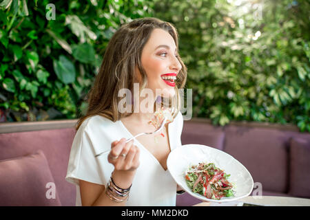 Junge und schöne Frau mit gesunden Salat an das vegetarische Restaurant sitzen mit Living Wall der grünen Pflanzen drinnen. Gesunde Ernährung Konzept Stockfoto