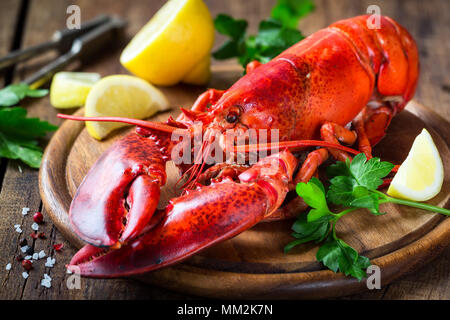 Gedünsteter Red Lobster auf einer hölzernen Schneidebrett mit Petersilie und Zitrone Stockfoto