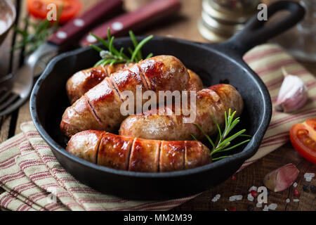 Gegrillte Würstchen oder Knallkörper in Gusseisen Skillet oder Pfanne mit Tomaten, Knoblauch und Rosmarin Stockfoto