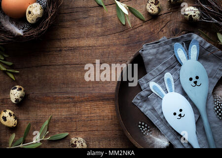 Ostern Rahmen für Werbebanner oder Grüße. Wachteleier, olivenzweige und eine hölzerne Platte mit Osterhase dekorativer Löffel gegen rustikalen Hintergrund Stockfoto