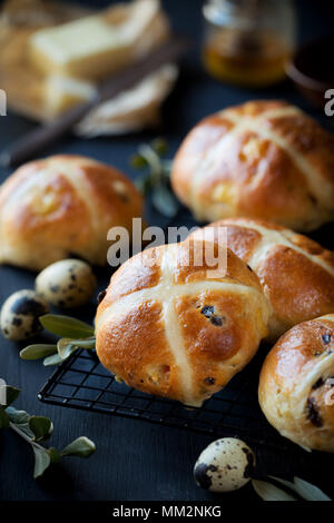 Frisch gebackene Hot Cross Buns auf einem Gitter mit Butter und Honig im Hintergrund Stockfoto