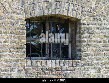 Alte Fenster mit Bars auf einem gelben Backsteinmauer zu renovieren Stockfoto