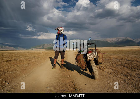 Motorrad reisenden Mann in Helm mit Koffer stehen auf extreme Rocky Road in einem Bergtal in Wetter auf dem Hintergrund der endlosen St Stockfoto