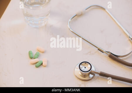 Apotheke Hintergrund auf einem weißen Tisch. Tabletten auf einem weißen Hintergrund. Pillen. Medizin und gesund. Nahaufnahme von Kapseln. Stethoskop auf weißem Holz- Stockfoto