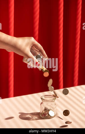 Eine weibliche Hand halten eine Münze, und setzen Sie sie in Glas Stockfoto