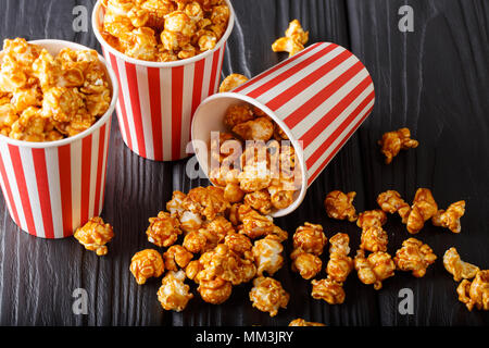 Lecker Popcorn mit Karamell in Papier Schaufel auf hölzernen Tisch gegen den dunklen Hintergrund. Horizontale Stockfoto