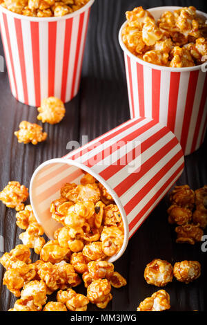 Karamell Popcorn in gestreiften box close-up auf Holz- Hintergrund. Vertikale Stockfoto