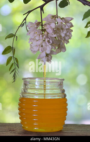 Glas gießen Honig mit Blumen von Akazienholz auf Tisch Stockfoto