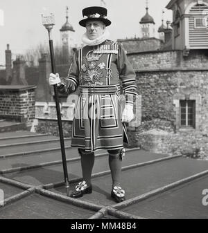 1950, historische, eine yeoman Warder der Festung des Tower von London, um die Aufmerksamkeit auf eine Dachterrasse am Turm in voller Tudor, Kleid, mit dem Stab in der Hand, London, England, UK. Die Yeomen warders wurden im Jahre 1485 von König Heinrich VII., der erste Monarch der Tudor-dynastie erstellt. Stockfoto