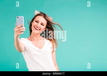 Glücklich lächelnde blonde Teen Girl macht selfie per Smartphone auf blauem Hintergrund Stockfoto