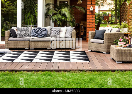 Rattan Sofa und Sessel mit Kissen auf einer Holzterrasse von einem modernen Haus Stockfoto