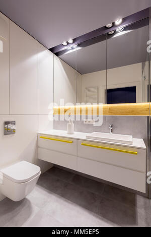 Spiegel und Leuchten über dem Waschbecken und ein Schrank mit gelben Akzenten im modernen Bad Stockfoto