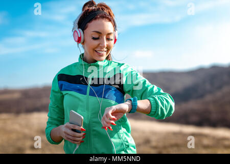 Junge sportliche Frau mit Kopfhörer auf der Suche nach einer Stoppuhr vor dem Training in der Natur. Stockfoto