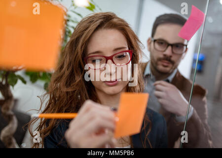 Kreative weibliche Fachleute Executive stehen im Büro hinter einer Glaswand mit Haftnotizen. Stockfoto