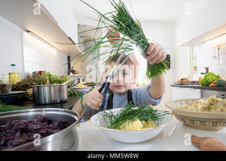 Little Boy schneiden frische organische Schnittlauch in der Küche Stockfoto