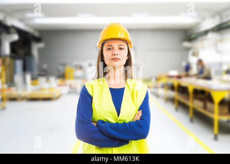 Stolz, selbstbewussten jungen Frau Ingenieur mit Waffen als professionelle Supervisor Konzept auf Indoor factory Hintergrund gekreuzt Stockfoto