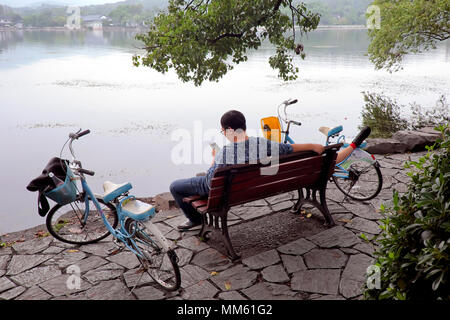 Man Surfen / sein Handy prüfen, während seine Freundin nimmt eine Power Nap, West Lake, Hangzhou, Provinz Zhejiang, China Stockfoto