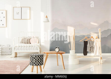 Sonne scheint auf eine Landschaft wallpaper von Schlafzimmer ist eine stilvolle kleine Mädchen Interieur mit Kleidung auf eine kreative und funktionelle Holz Kleiderbügel Stockfoto