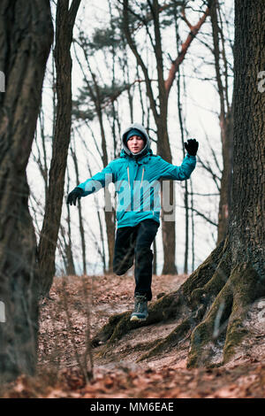 Junge Mann laufen im Freien während des Trainings in einem Wald unter blattlosen Bäume auf kalten freeze Herbst Tag. Junge trägt Sport Kleidung Stockfoto