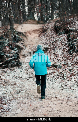 Junge Mann laufen im Freien während des Trainings in einem Wald unter kahlen Bäumen an einem kalten Tag im Winter einfrieren. Junge trägt Sport Kleidung Stockfoto