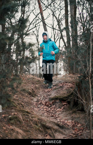 Junge Mann laufen im Freien während des Trainings in einem Wald unter blattlosen Bäume auf kalten freeze Herbst Tag. Junge trägt Sport Kleidung Stockfoto