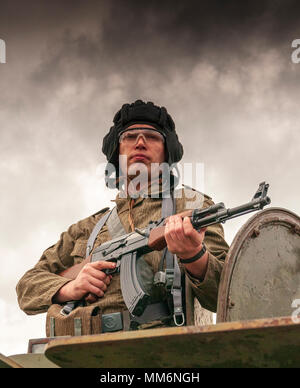 Eine airsoft Spieler tragen von Ostdeutschen, Junior Non-Commissioned Officers Uniform mit einer AK-47 von einem Bdrm sowjetische gepanzerte Fahrzeug stand Stockfoto