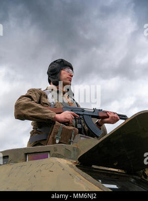 Eine airsoft Spieler tragen von Ostdeutschen, Junior Non-Commissioned Officers Uniform mit einer AK-47 von einem Bdrm sowjetische gepanzerte Fahrzeug stand Stockfoto