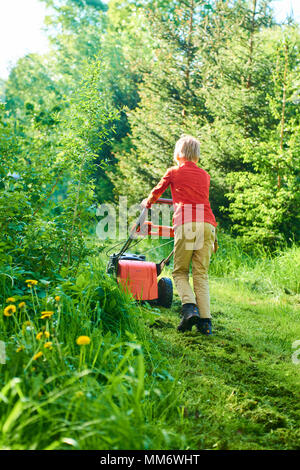 Kind Junge Helfen im Garten mähen Rasen mit einem Rasenmäher Stockfoto