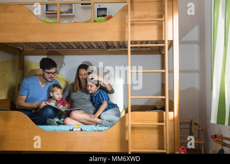 Vater und der schwangeren Mutter ein Buch zu lesen um ihre zwei Söhne auf Etagenbett, München, Deutschland Stockfoto